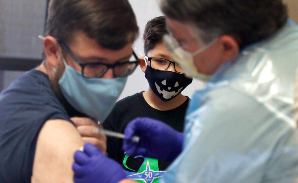 Kurt Price, 7, watches as his step-father, Scott Hammell, an instructional assistant at Adams Elementary School, gets his COVID-19 vaccine shot during a mass vaccine event at Wake County Commons Building in Raleigh, N.C., Wednesday, February 24, 2021. Wednesday was the first day preK-12 public, private and charter schools, as well as childcare workers, became eligible to begin getting shots.