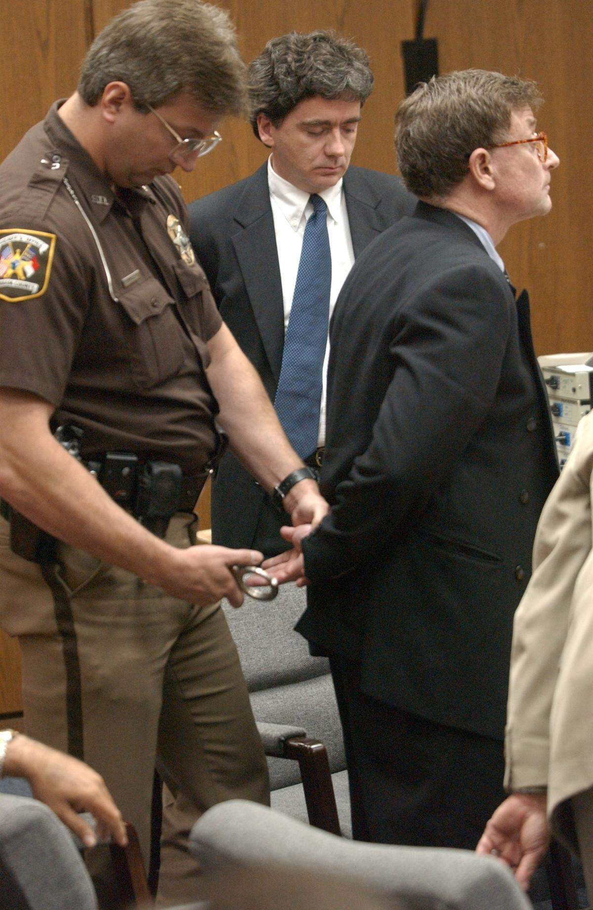 Durham Co. Sheriff’s deputy Bryan Mister, left, puts the handcuffs on convicted murderer Michael I. Peterson, right, with defense attorney Thomas Maher shortly after the Peterson jury returned its first degree murder verdict of guilty at 1055 am Friday in Durham Superior court.