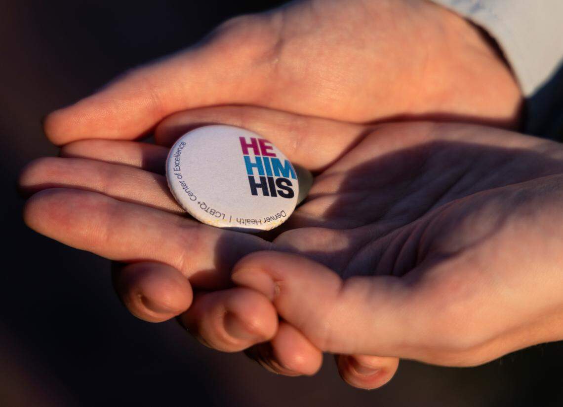 Dr. Riley Smith, pictured on Tuesday, August 1, 2023, in Chapel Hill, N.C., holds a pronoun pin that he wears on a lanyard while working. Dr. Smith practices family medicine and provides gender-affirming care.