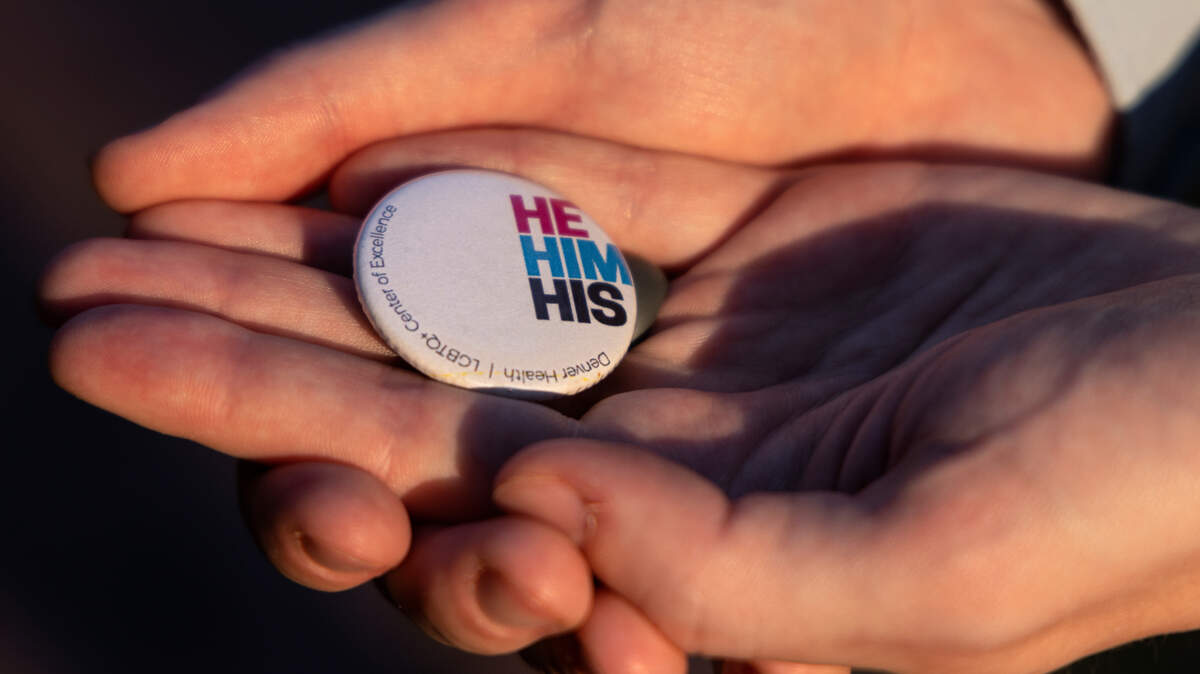 Dr. Riley Smith, pictured on Tuesday, August 1, 2023, in Chapel Hill, N.C., holds a pronoun pin that he wears on a lanyard while working. Dr. Smith practices family medicine and provides gender-affirming care. 