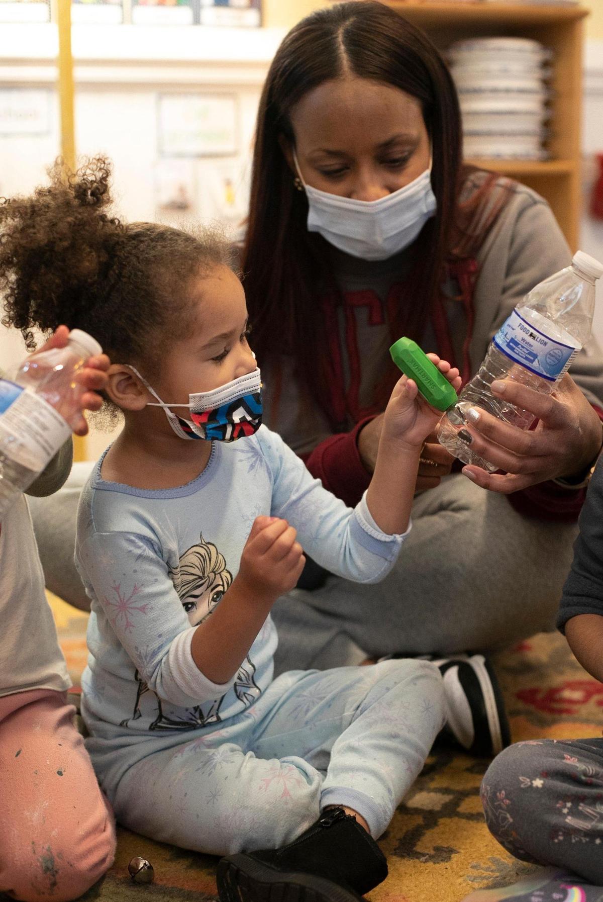 Teacher Nikki Pendleton shows three-year-old Ayla Adamas how to use a magnet to move a bell inside a plastic bottle during music class at A Safe Place Child Enrichment Center on Tuesday, December 20, 2022 in Raleigh, N.C.
