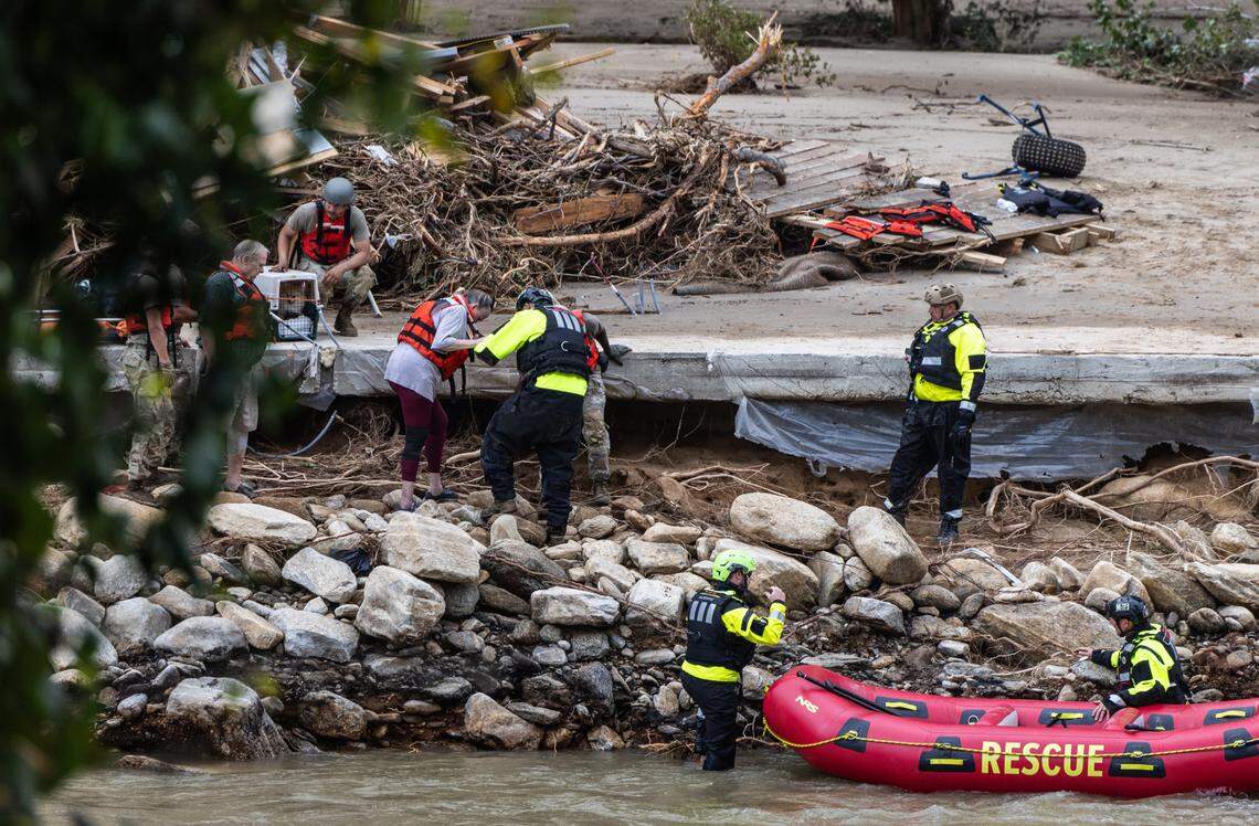 Two people and a dog are escorted to a rescue boat in Chimney Rock, N.C. on Sunday, September 29, 2024.