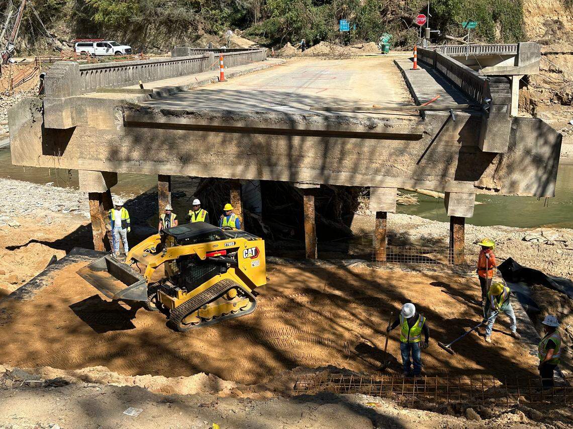 Workers layer in soil to fill a gap between bank of Rocky Broad River and the U.S. 64 bridge in Bat Cave, North Carolina, on Thursday, Oct. 10, 2024. The deluge from Hurricane Helene two weeks earlier carried away soil and riprap, severing the main highway connection into the community.
