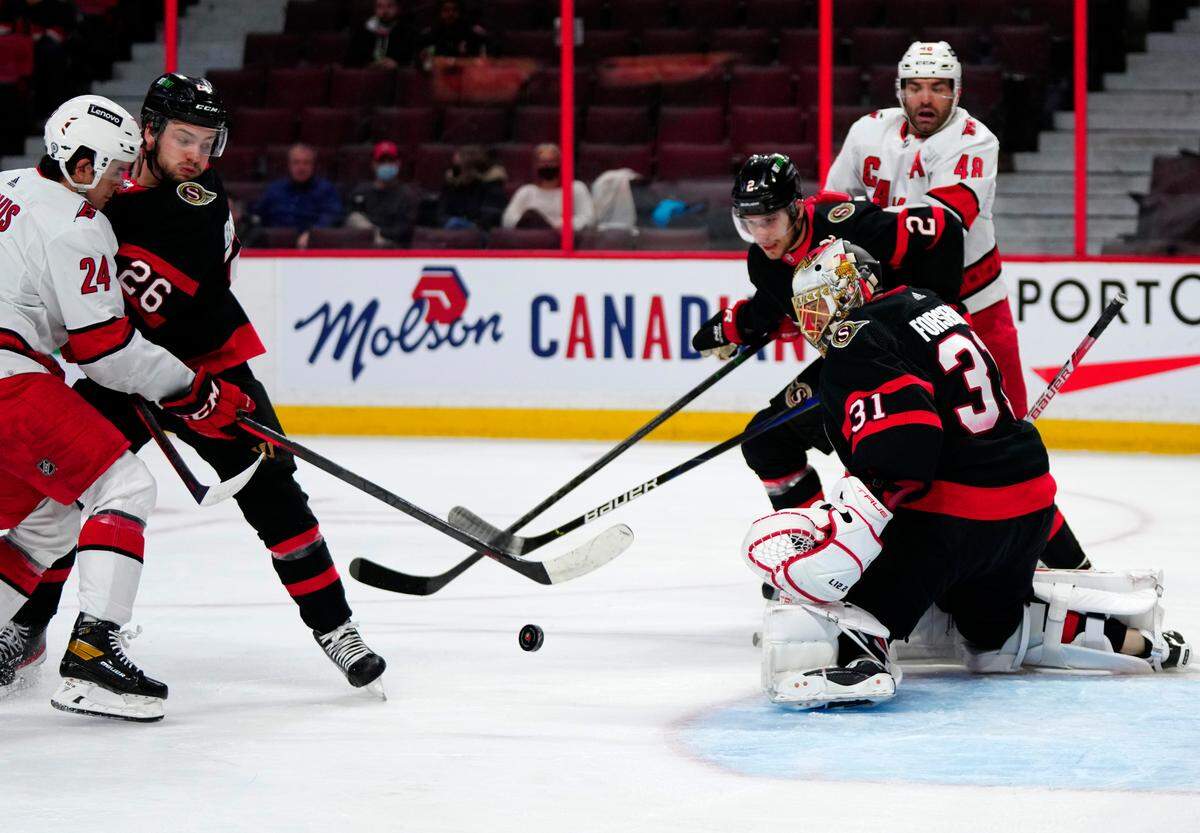 Ottawa Senators goaltender Anton Forsberg (31) keeps his eye on the puck as defenceman Erik Brannstrom (26) keeps Carolina Hurricanes center Seth Jarvis (24) away during the first period of an NHL hockey game Tuesday, Feb. 8, 2022, 2022 in Ottawa, Ontario. (Justin Tang/The Canadian Press via AP)