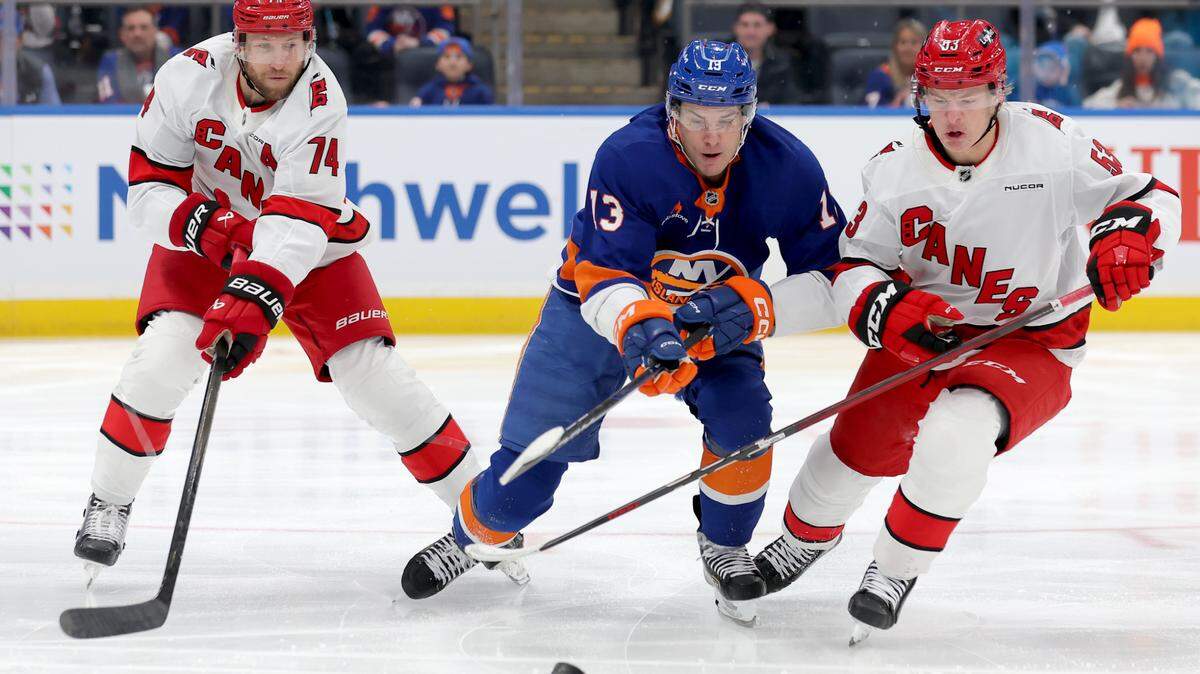 New York Islanders center Mathew Barzal (13) fights for the puck against Carolina Hurricanes defenseman Jaccob Slavin (74) and right wing Jackson Blake (53) during the first period at UBS Arena.