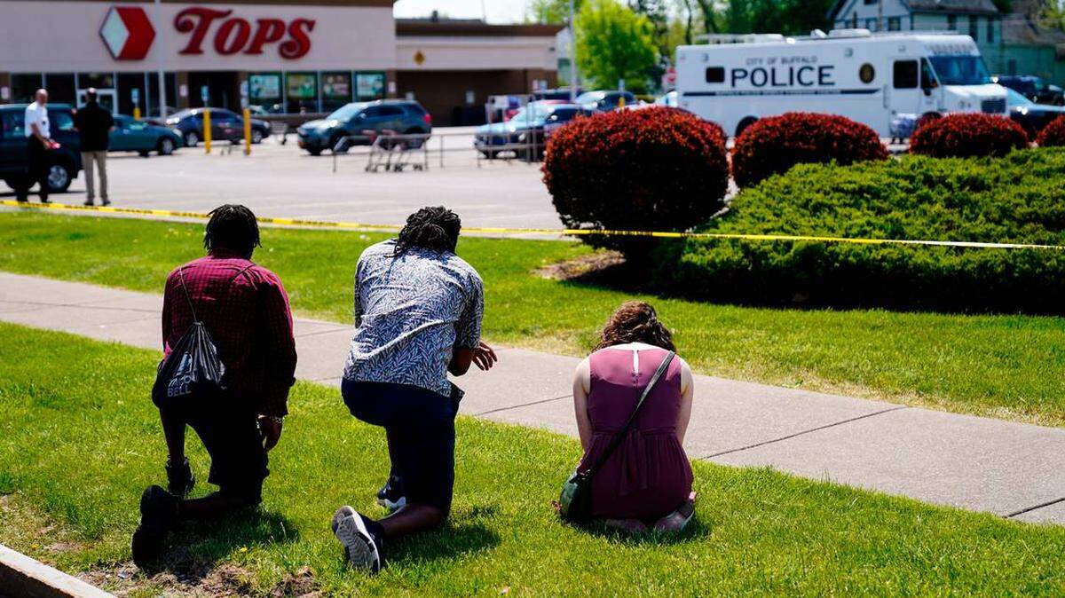 People pray outside the scene of the Buffalo, N.Y. mass shooting at a Tops supermarket on May 15, 2022 that left 10 Black people dead.