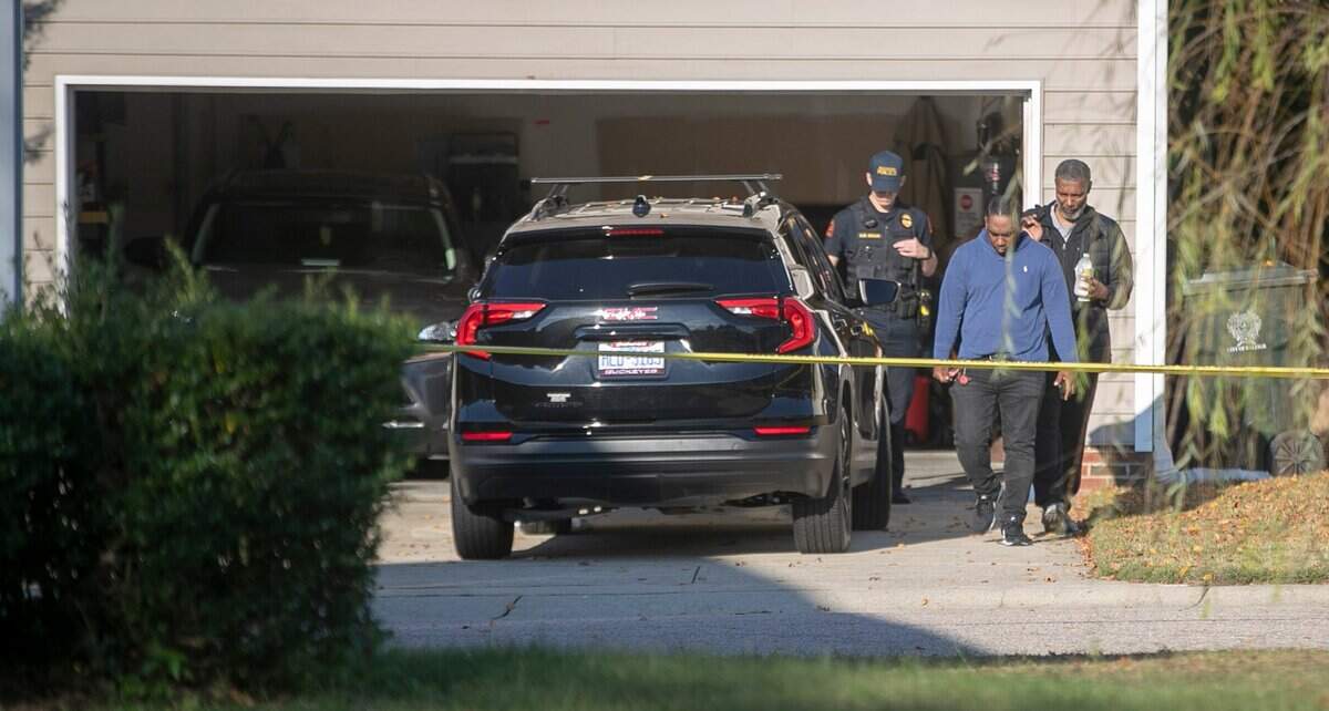 Police escort unidentified men out of the garage at 5355 Sahalee Way on Friday morning, October 14, 2022 in Raleigh, N.C. as they continue to investigate the killing of five people yesterday on the greenway nearby.