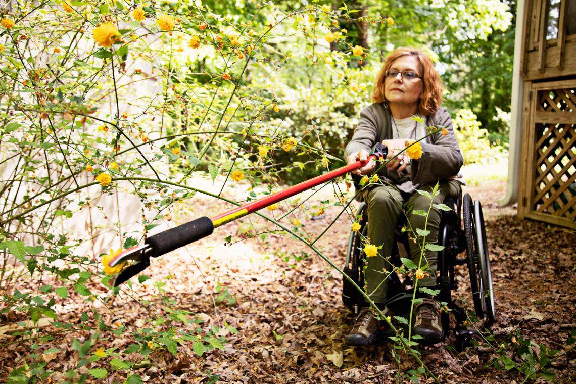 Pam Dickens uses a trimmer with an adjustable handle to reach high branches that need a bit of pruning in her Hillsborough yard on Friday, April 29, 2022. Dickens uses a variety of tools with adjustable handles that allow her to work with ease from her wheelchair while gardening.
