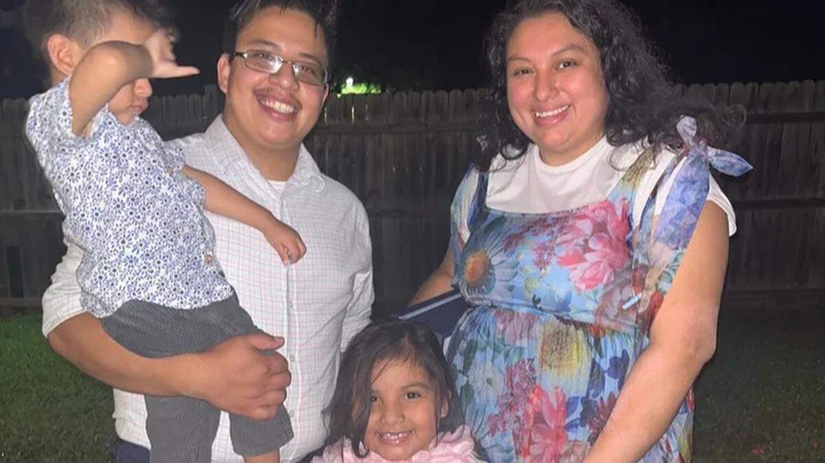Moises Benitez Diaz is holding his son, Elijah, while wearing a white-checkered button down shirt and glasses with a black frame. He stands next to his wife, Esmeralda Escobar, wearing a white shirt under her blue dress with pink, yellow and blue flowers. In the middle is the couple’s daughter, Rochelle.