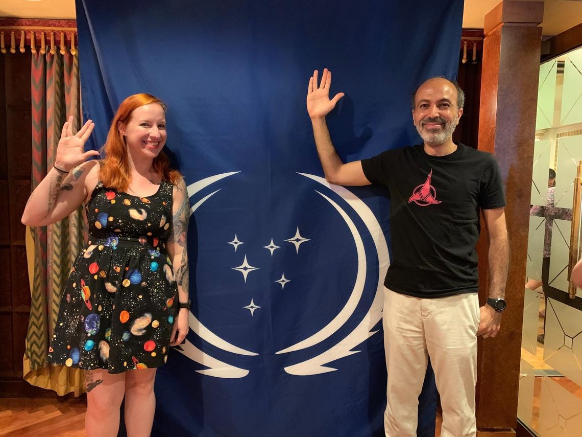 Erin MacDonald (left) and Mohamed Noor (right) pose for a picture in front of the Federation flag during “Star Trek: The Cruise IV” in March 2020. They’re the newest scientific consultants on the “Star Trek” franchise.