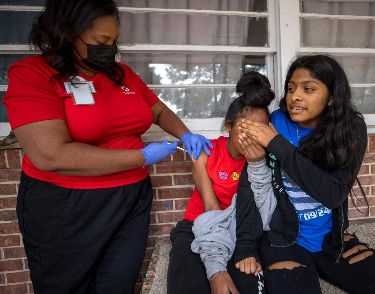 Fifteen-year-old Emily Gutierrez comforts her 13-year-old sister Eily Gutierrez, as Dr. Nerissa Price administers the COVID-19 vaccine on the porch of the family home on Friday, October 8, 2021, in Raleigh, N.C.