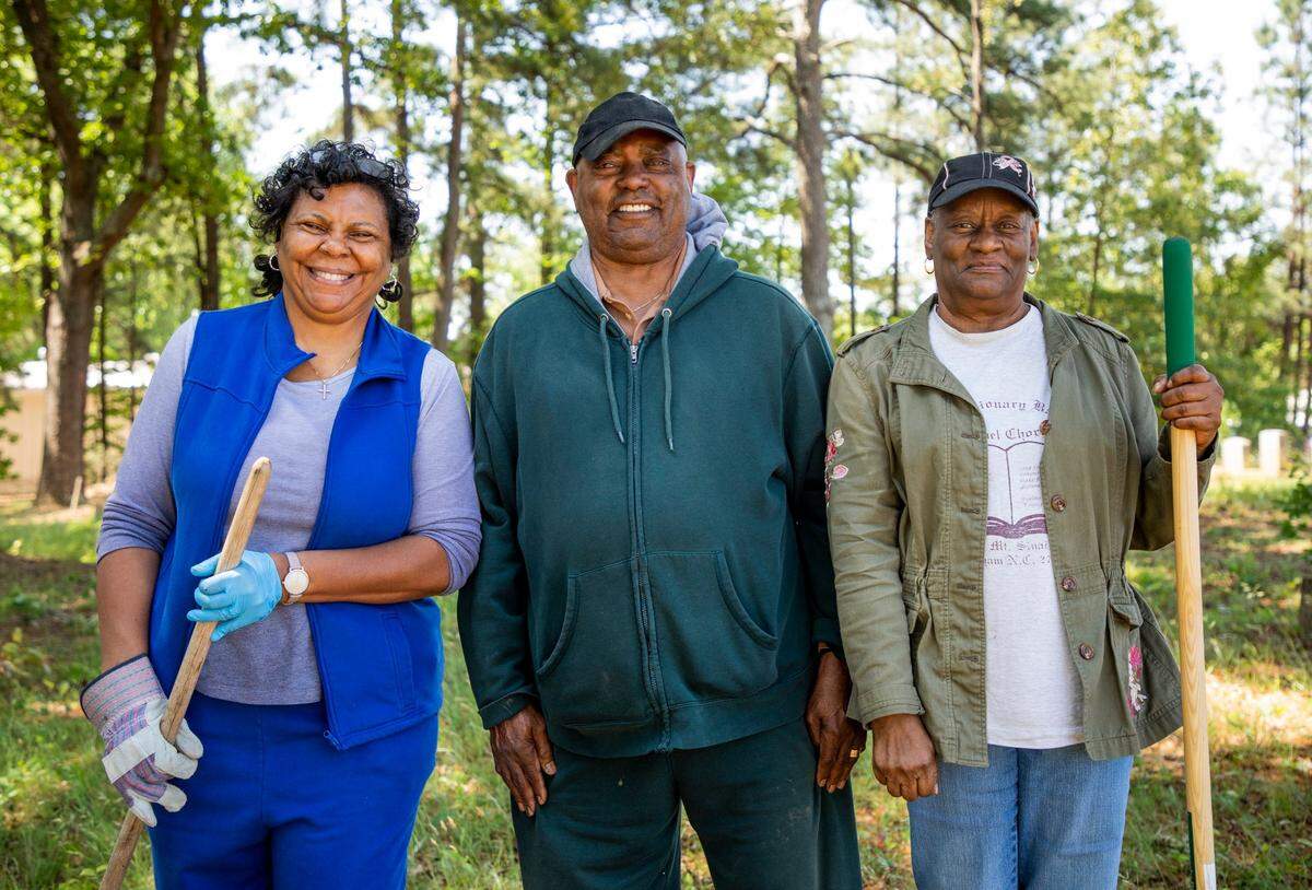 From left, Deborah Lofton, Clement Harris, and Ethel LaVerne Patterson stand for a portrait after cleaning the graves of their family members in the Oak Grove Cemetery, which was founded by freed African-Americans after the Civil War and now has lost more of its tree buffer to widening of the I-440 Beltline, that separated it from the rest of the Method community in the 1960s, on Saturday, May 8, 2021, in Raleigh, N.C.