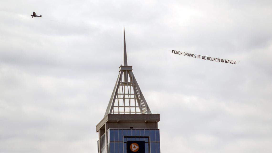A plane with a banner that reads “Fewer graves if we reopen in waves” circles downtown Raleigh during a ReOpen NC rally Tuesday, May 12, 2020.