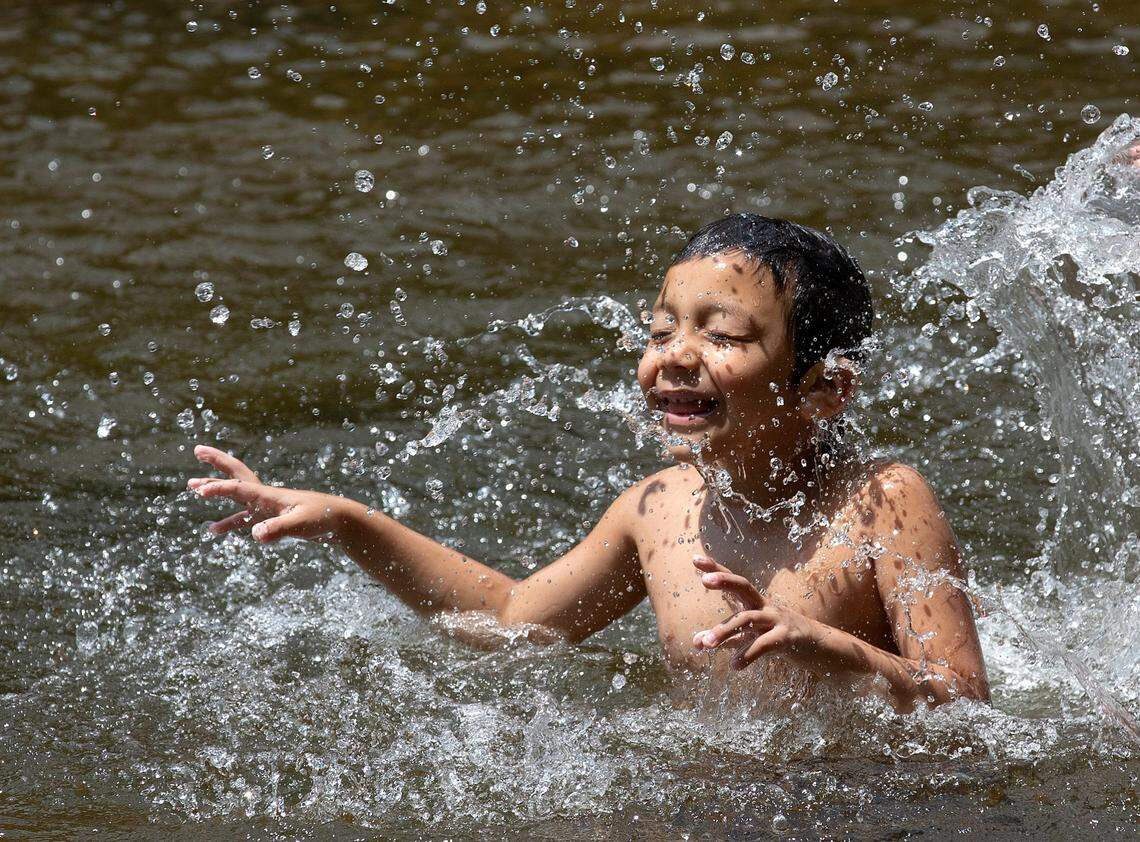 Omar Martinez, 6, smiles while splashing in the water at West Point on the Eno on Monday, June 24, 2024, in Durham, N.C.