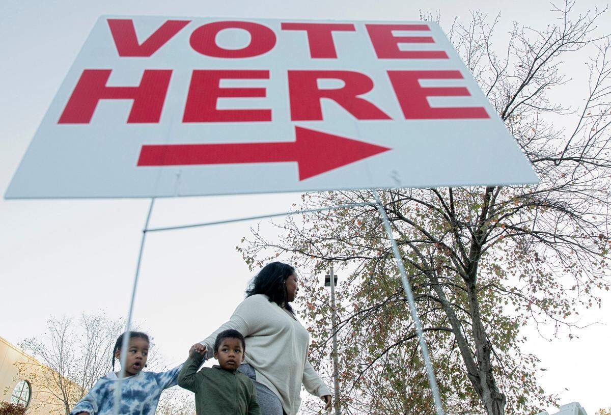 Brittany Jordan walks with her children, Giselle, 2, and Ralphael, 3, past a voting sign outside of Monument of Faith Church on Tuesday, Nov. 8, 2022, in Durham, N.C.