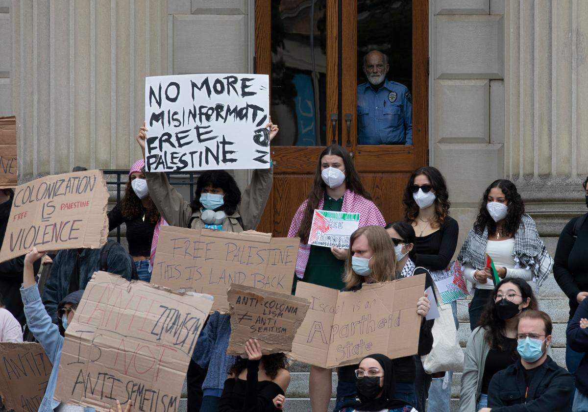 A person looks out from Wilson Library as people hold signs during a rally in support of Palestinians at UNC-Chapel Hill on Thursday, Oct. 12, 2023.