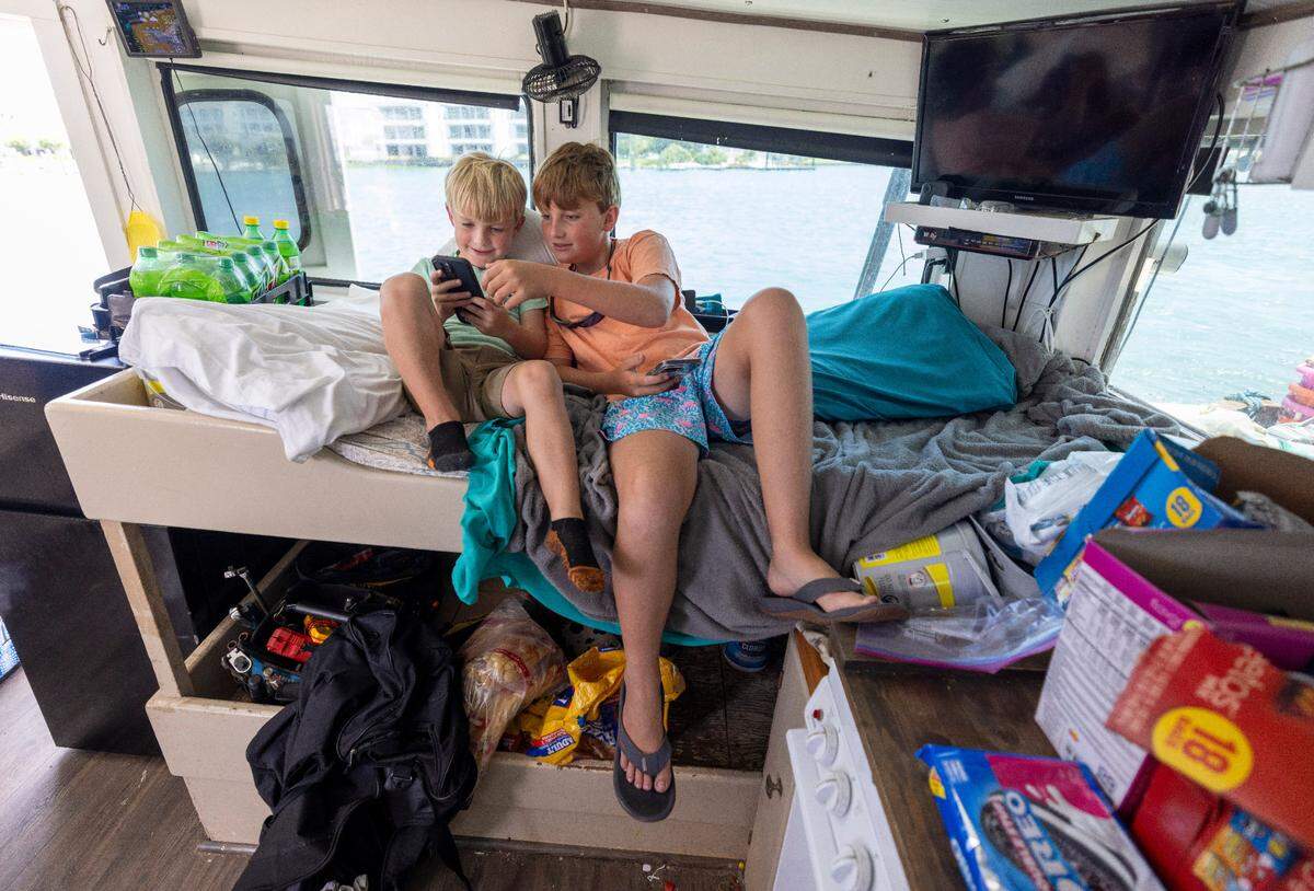 Connor Smith, 5, brother Cameron Smith, 12, play on their phones aboard the shrimper Della John while it is offloaded with fresh caught shrimp at Beaufort Inlet Seafood on Thursday, July 17, 2025 in Beaufort, N.C.