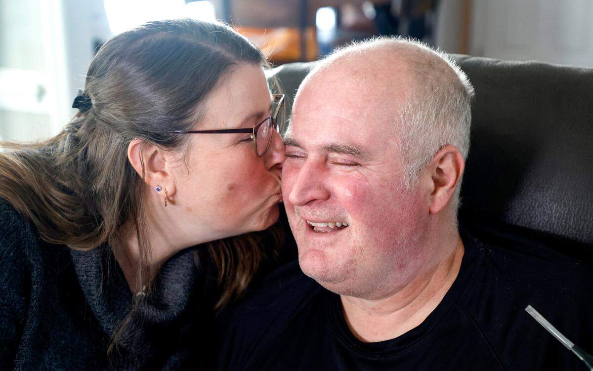 Jamie Woodlief gives her husband Roy as kiss while posing for a portrait in their home in Garner, N.C., on Friday, Jan. 17, 2025. Roy has been diagnosed with amyotrophic lateral sclerosis (ALS), forcing him to retire from the Wake County Sheriff’s Office. The fatal disease causes muscle weakness, making it difficult to walk, eat and eventually breathe.