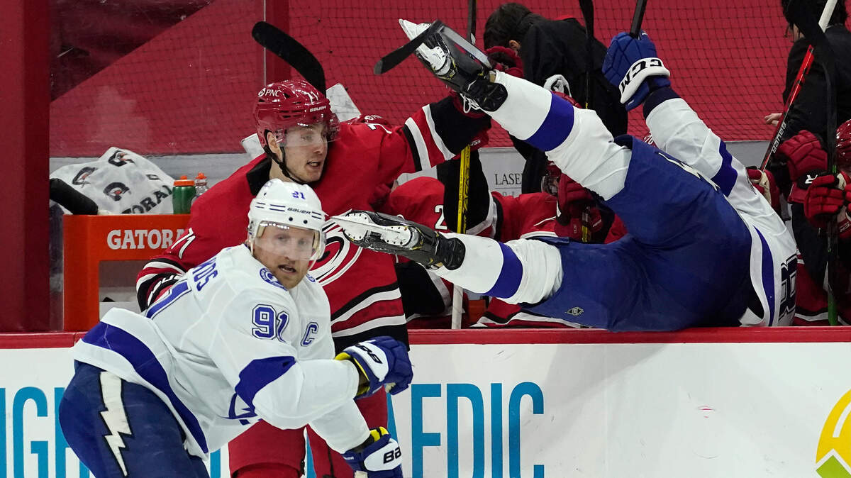 Tampa Bay Lightning defenseman Erik Cernak, of Slovakia, falls into the bench area as center Steven Stamkos (91) and Carolina Hurricanes right wing Jesper Fast (71), of Sweden, skate during the second period of an NHL hockey game in Raleigh, N.C., Monday, Feb. 22, 2021. (AP Photo/Gerry Broome)