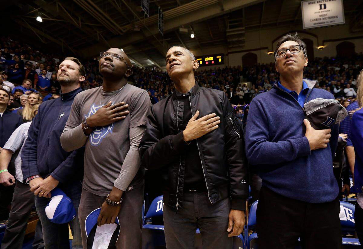 Former President Barack Obama joins fans while the national anthem is played during an NCAA college basketball game between Duke and North Carolina in Durham, N.C., Wednesday, Feb. 20, 2019. (AP Photo/Gerry Broome)