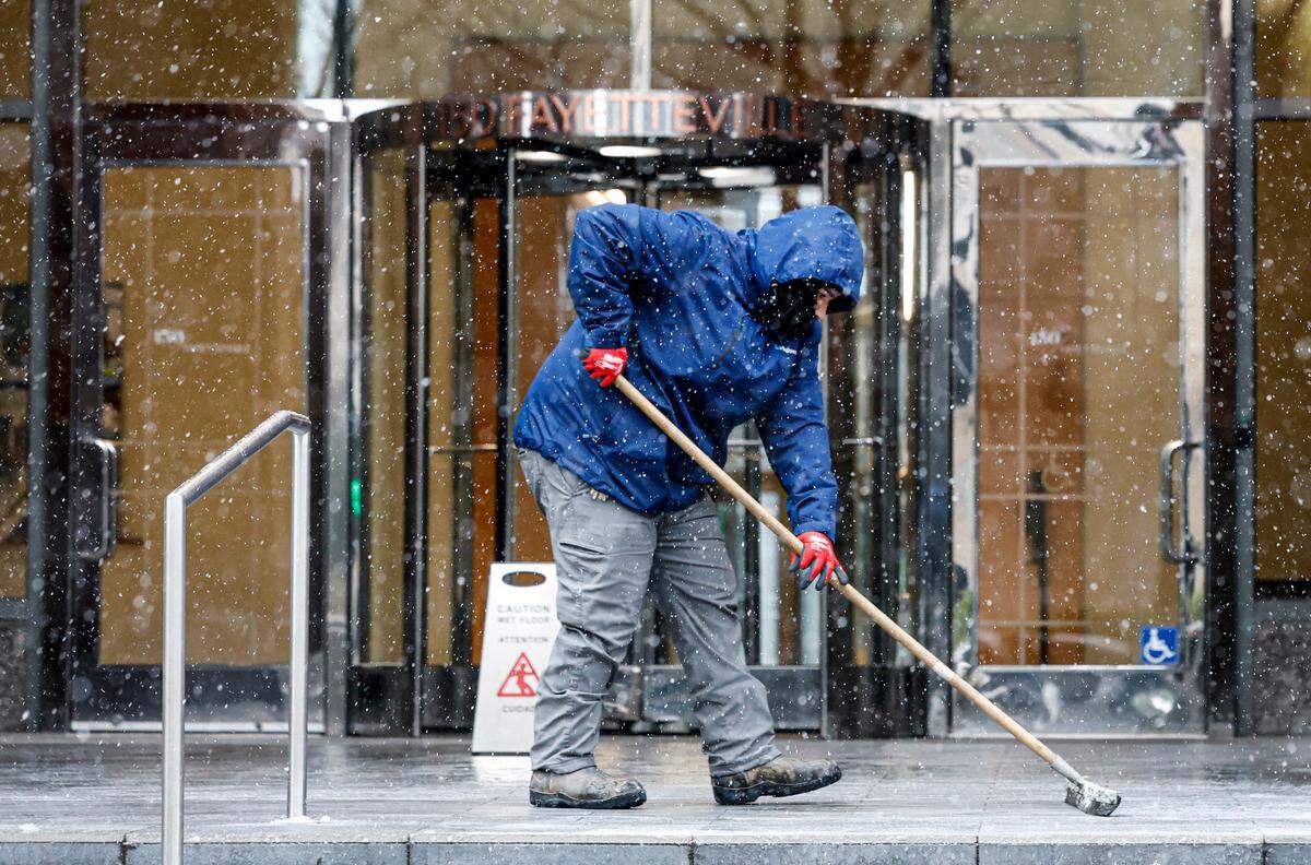 Nidhal Benyahia with Highwoods Properties clears the snow and slush from an entrance to 150 Fayetteville in downtown Raleigh early Wednesday afternoon, Feb. 19, 2025.