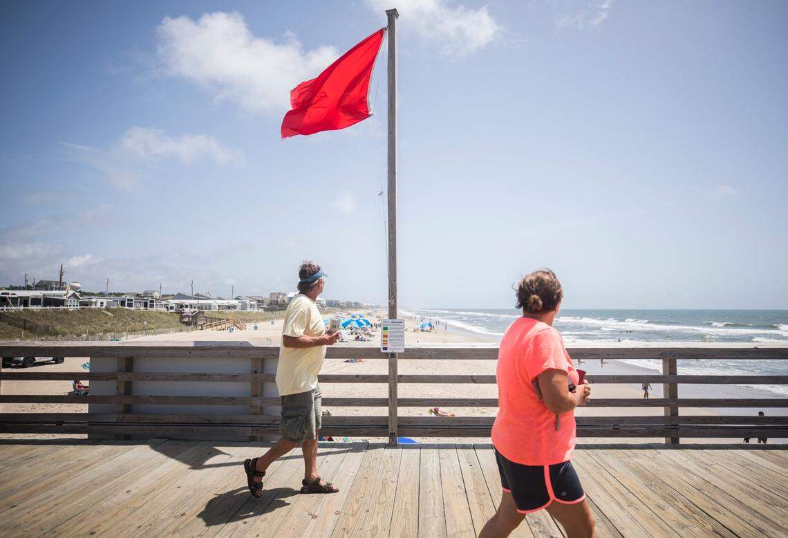 Patrons of the Bogue Inlet Pier in Emerald Isle, N.C. walk past a red flag signaling hazardous swimming conditions as Tropical Storm Isaias approaches the southeast on Sunday, Aug. 2, 2020.