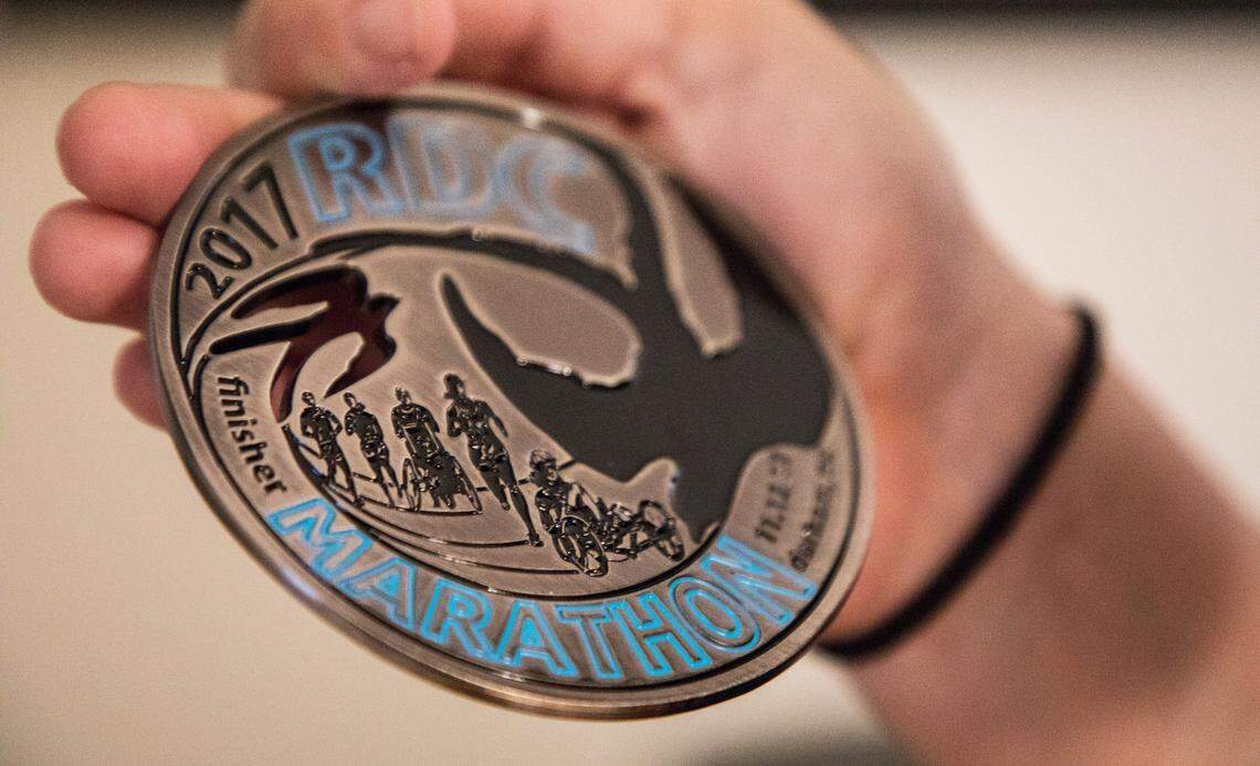 Andrea Peet points out an engraving of her on a recumbent trike on a marathon medal she received in 2017, in her home in Raleigh, N.C. on Feb. 13, 2020. Peet’s latest goal is to compete in a race in all 50 states. She has completed 20 races to date.