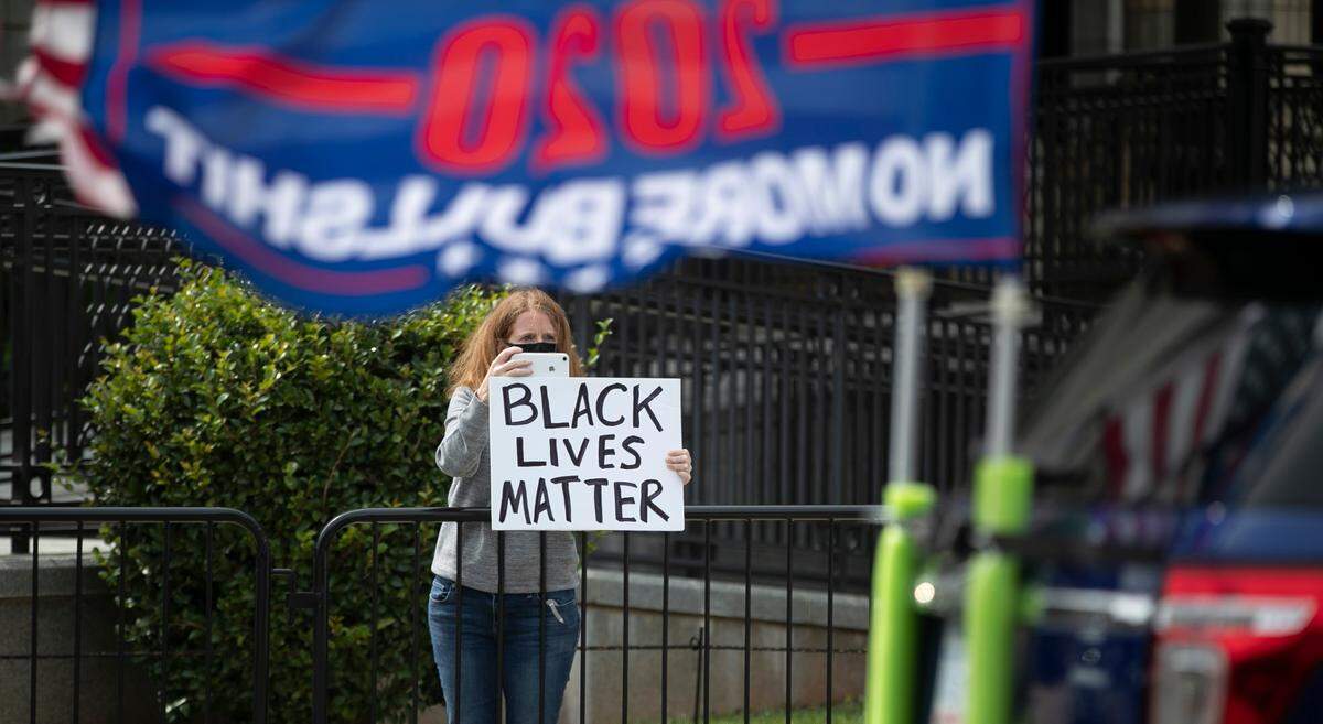 Elon University professor Megan Squire displays a Black Lives Matter sign as she records a parade of Trump supporters at the Alamance County Courthouse in Graham, N.C. on Saturday, September, 19, 2020.