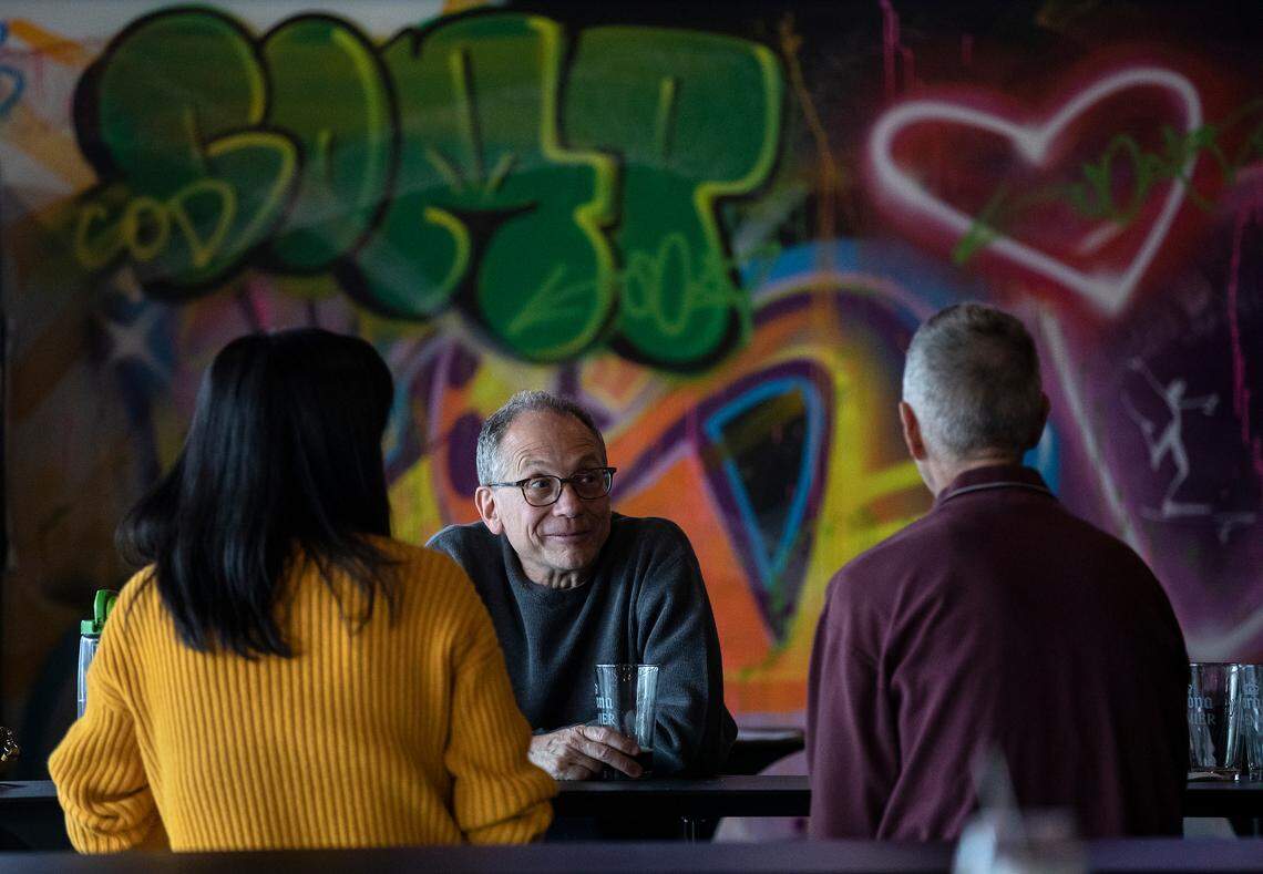 Robert Saccoccio, center, stands next to a wall of art inside Graffiti: Spirits, Axes & Art in Cary, N.C. on Thursday, March 16, 2023.