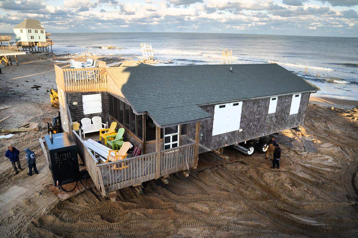 House movers slowly relocate the Buxton beach house of Lat and Debby Williams.  The couple bought the house from Debby’s parents, who had owned it since 1981. When they retired in 2017, the Williamses settled there full-time — then three rows back from the ocean. Now, with severe erosion threatening the property, their single-story house is being relocated in two stages: first to safety away from the surf, then to a new lot five blocks inland.