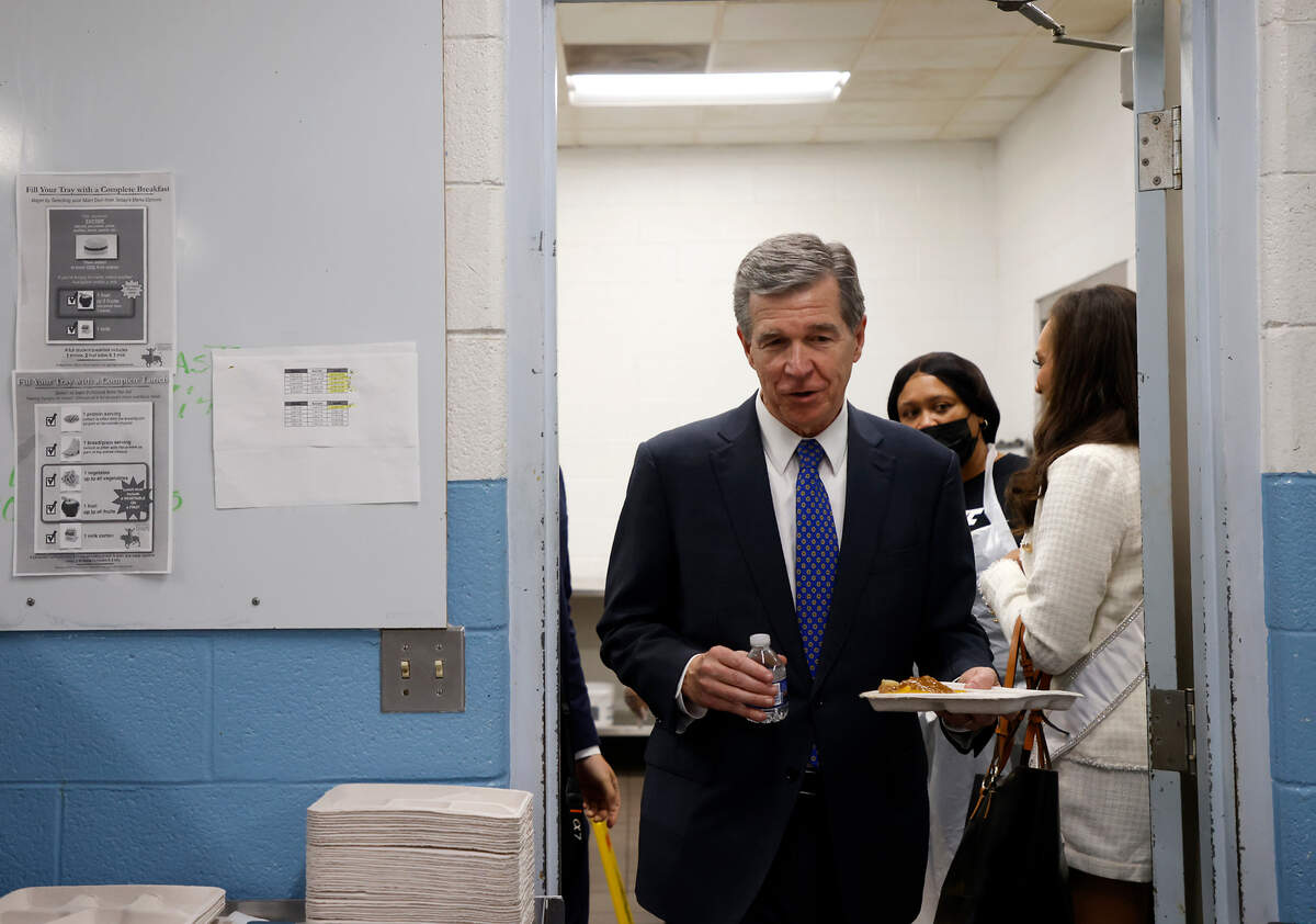 Gov. Roy Cooper carries a lunch tray into the cafeteria at Bethesda Elementary School on Tuesday, Oct. 11, 2022, in Durham, N.C. Cooper visited the school to announce new agreements to bring food from North Carolina farmers and producers to schools.