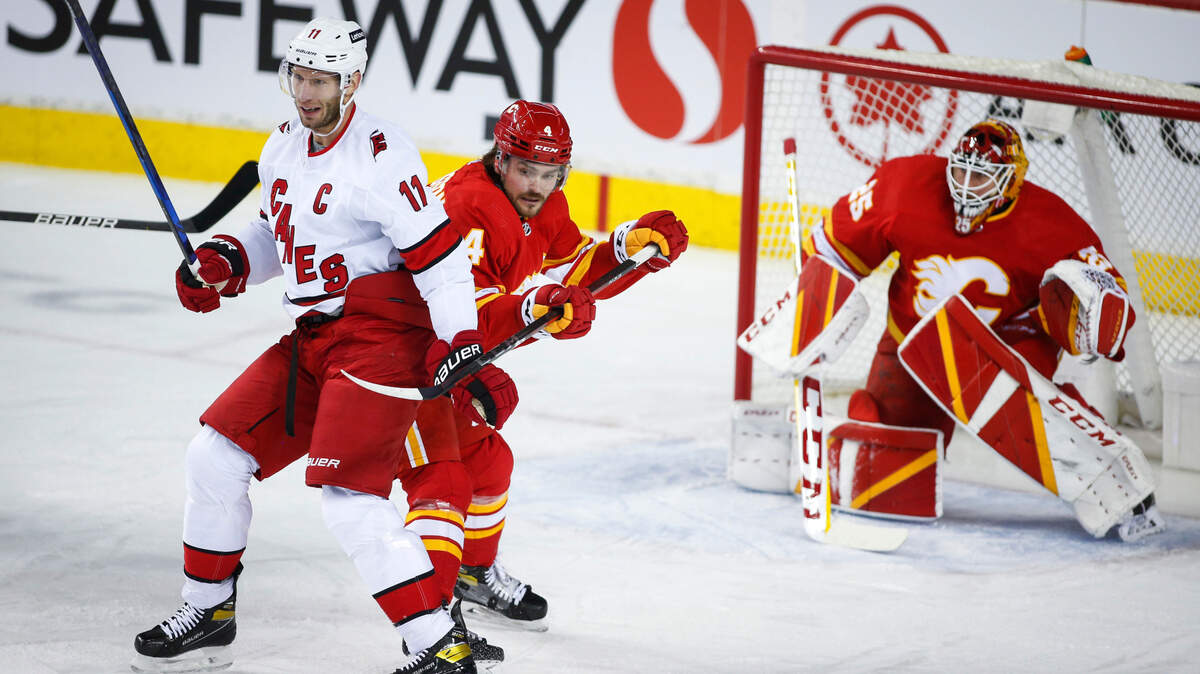 Carolina Hurricanes’ Jordan Staal, left, is checked by Calgary Flames’ Rasmus Andersson as goalie Jacob Markstrom watches during the first period of an NHL hockey game Thursday, Dec. 9, 2021, in Calgary, Alberta. (Jeff McIntosh/The Canadian Press via AP)