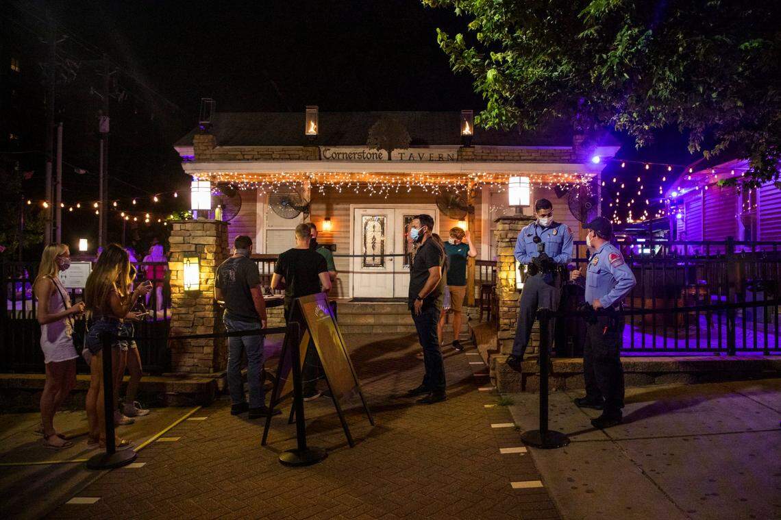 Two Raleigh police officers stand outside the Cornerstone Tavern on Glenwood Avenue, which opened its doors for business despite Gov. Roy CooperÕs veto of legislation to reopen bars and a judgeÕs decision hours earlier denying a lawsuit brought against the governorÕs executive orders by the N.C. Bar and Tavern Association, on Friday, Jun. 26, 2020, in Raleigh, N.C.