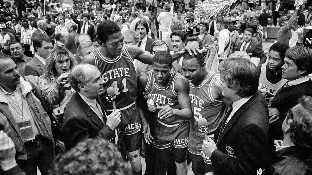 CBS announcer Billy Packer, left, interviews N.C. State seniors Thurl Bailey, Dereck Whittenburg, and Sidney Lowe after the Wolfpack won the National Championship on April 4, 1983. The Wolfpack won the game 54-52.