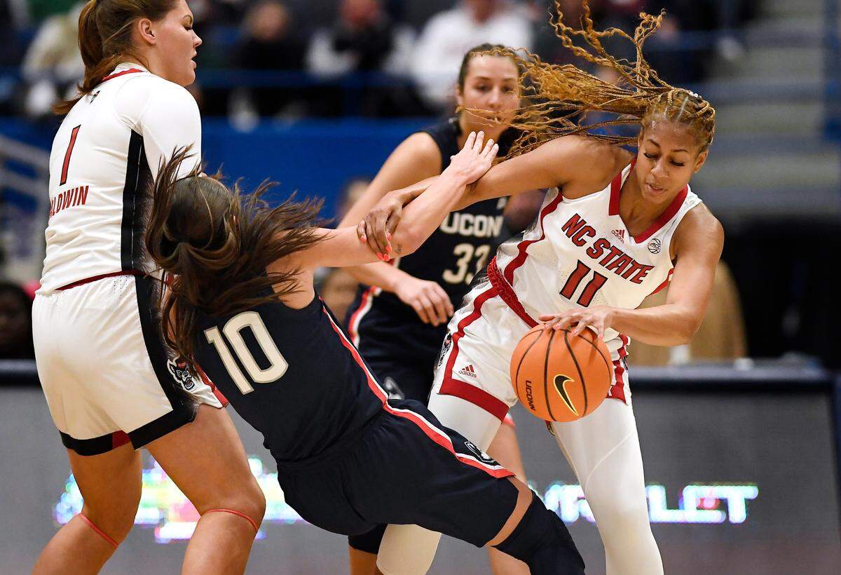 NC State’s Jakia Brown-Turner (11) fouls Connecticut’s Nika Muhl (10) during the first half of an NCAA college basketball game, Sunday, Nov. 20, 2022, in Hartford, Conn.