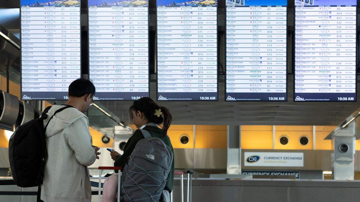 People stand in front of an arrivals and departures sign at Raleigh-Durham International Airport on Tuesday, Dec. 24, 2024.