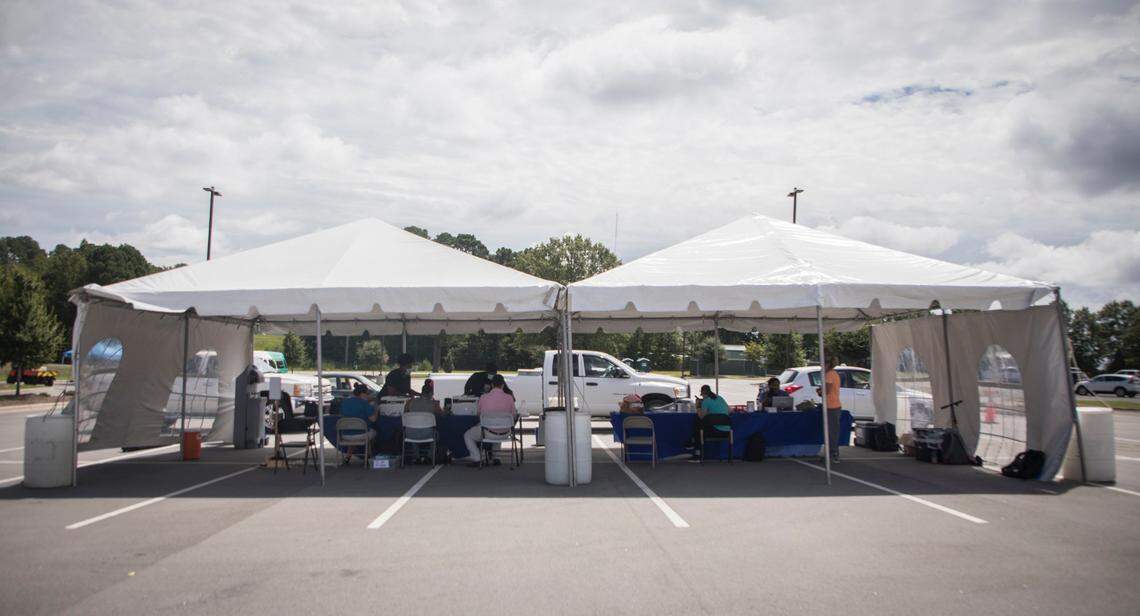 People begin lining up at two tents in the parking lot of the the Dennis A. Wicker Civic Center in Sanford, N.C. on Tuesday, Aug. 25, 2020 to check-in for free COVID-19 testing. The testing site, hosted by the UNC Health System, Lee County, and Piedmont Health Services, is one of many sites and events that have been setup to help people in rural counties get tested closer to home.