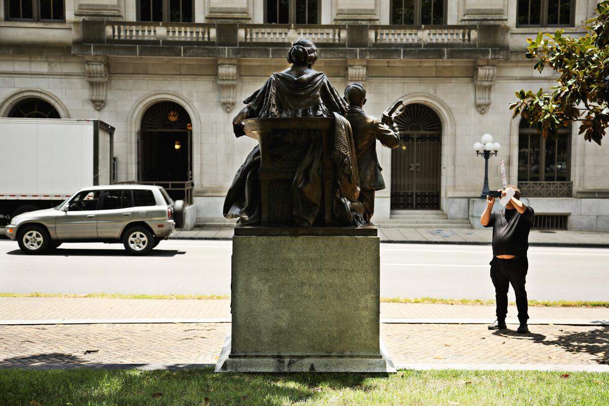 The Confederate Women’s Monument was dedicated June 10, 1914. The monument is a statue of a seated woman and a child — a boy holding a sword. It faces the street, and has two stone benches facing each other, flanking the monument.