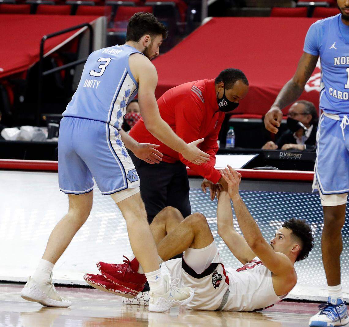 N.C. State head coach Kevin Keatts and North Carolina’s Andrew Platek (3) help up N.C. State’s Devon Daniels (24) during the second half of N.C. State’s 79-76 victory over UNC at PNC Arena in Raleigh, N.C., Tuesday, December 22, 2020.