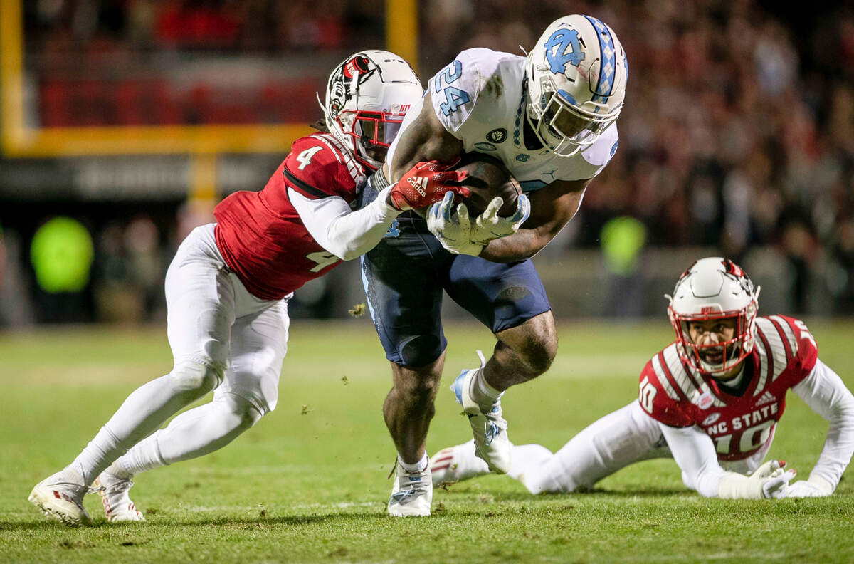 North Carolina’s British Brooks (24) breaks open for a 40-yard run in the first quarter as N.C. State’s Joshua Pierre-Louis (4) works to make the stop on Friday, November 26, 2021 at Carter-Finley Stadium in Raleigh, N.C.