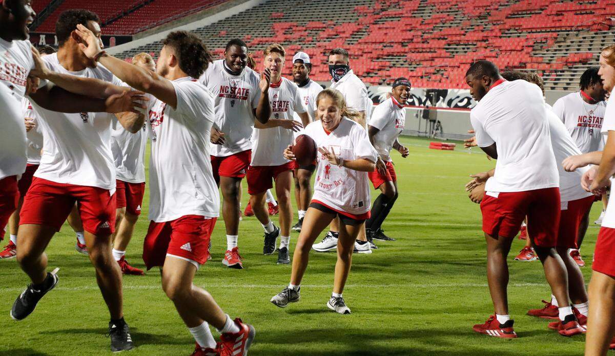 N.C. State football players clear a path for Grace Chalker as she runs for a touchdown during “Victory Day” with the Wolfpack at Carter-Finley Stadium in Raleigh, N.C., Saturday, August 7, 2021. The Wolfpack partnered with GiGi’s Playhouse Raleigh, a Down’s syndrome achievement center, to let participants enjoy a game day experience with players.
