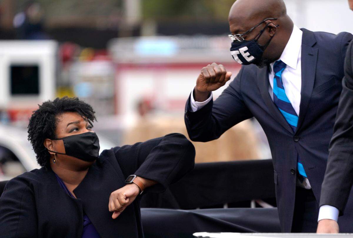 U.S. Democratic Senate candidate Raphael Warnock, right, bumps elbows with Stacey Abrams during a campaign rally with U.S. President-elect Joe Biden at Pullman Yard on Dec. 15, 2020 in Atlanta, Georgia.