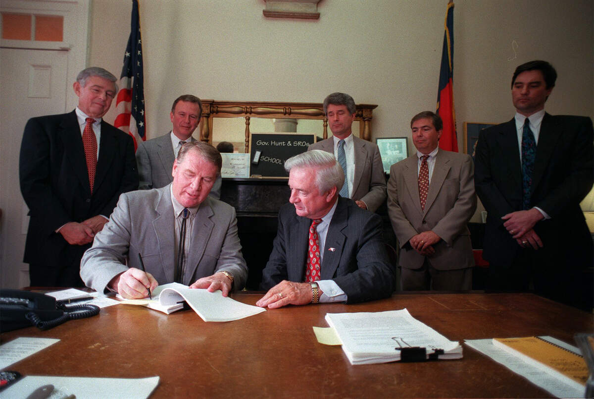 After inking his own signature, Gov. Jim Hunt (right) looks on as Steve Stroud (left) signs documents turning over state land to N.C. State for the new arena. Behind them are various state and N.C. State officials who participated in the 1997 deal.