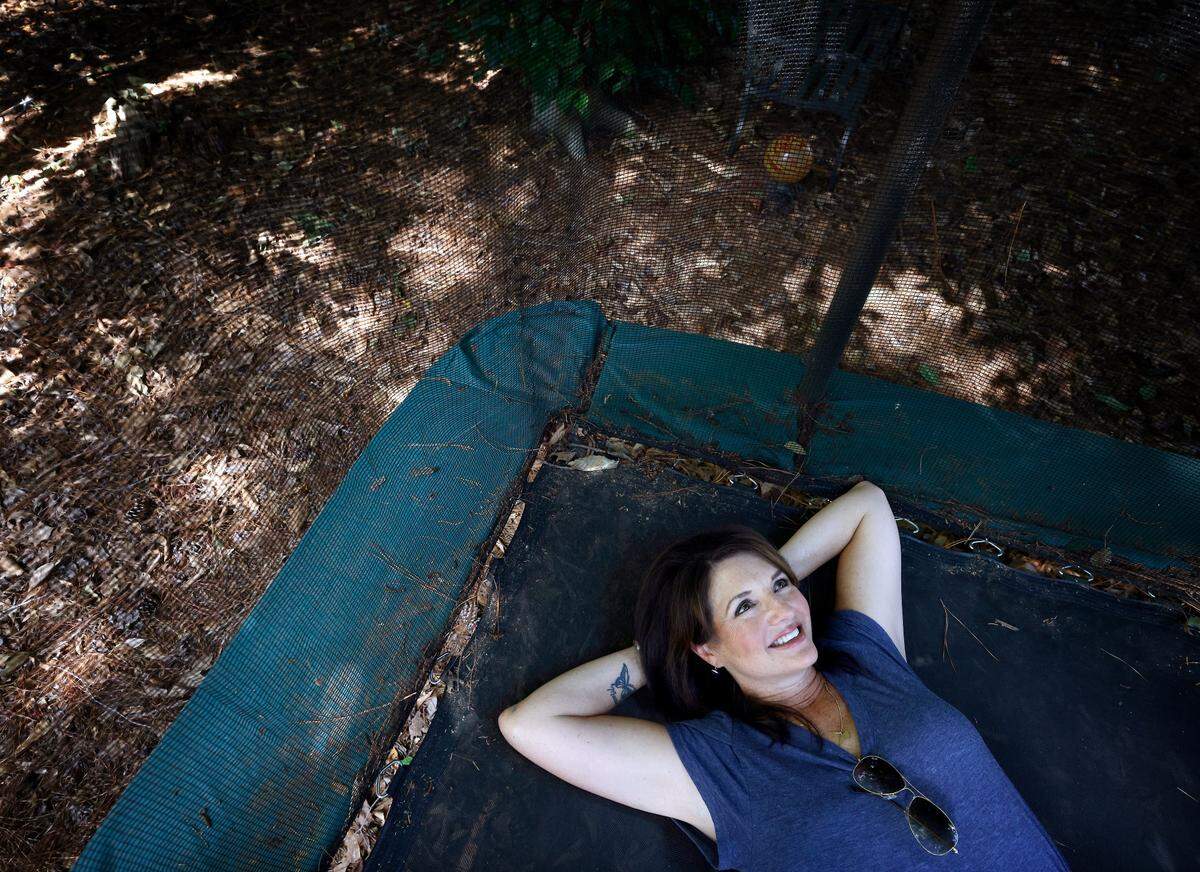 Sharon McCloud sits on a trampoline in the backyard of her Raleigh, N.C. home on Monday, August 8, 2022. After applying to have a trampoline in her yard in the fall of 2020, McCloud says she was initially told she’d have to get approval from her neighbors on its placement, despite having a play set in the same spot for 15 years. After documenting other trampolines in the neighborhood and speaking with neighbors about their experiences, the HOA approved her request.