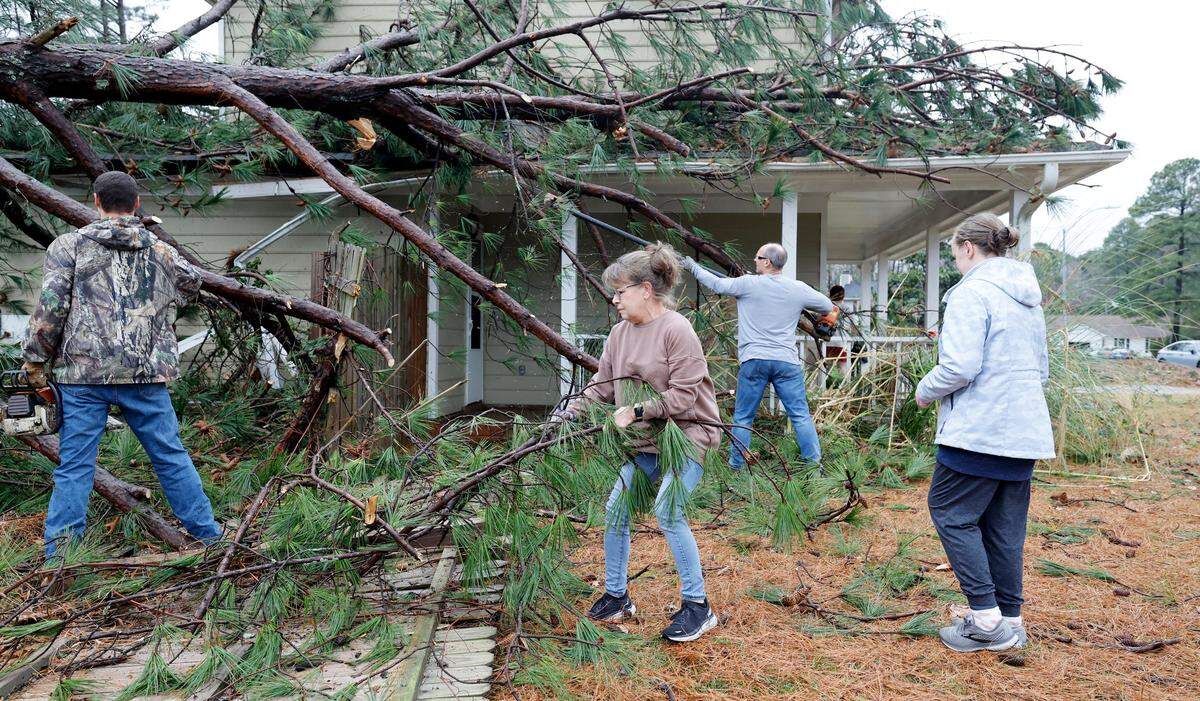 Lisa Stanley, center, and friends start to clean up knocked down trees that hit her son, Griffin’s, home on Buckhorn Road in Garner, N.C., Sunday, Dec. 10, 2023. Lisa said after the storm passed she texted her circle group from Holland’s Church and people showed up to help out. “What an awesome church family” said Stanley.
