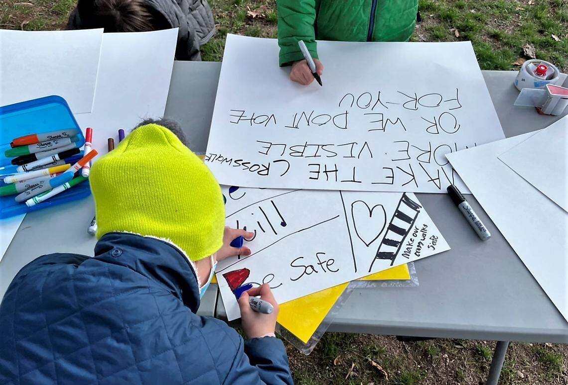 Children use markers and posterboard to make signs asking drivers to slow down and watch out for pedestrians. Well over 100 people crowded the sidewalks on Estes Drive on Friday, Jan. 7, 2022, as they walked to Franklin Street following a New Year’s Eve wreck.