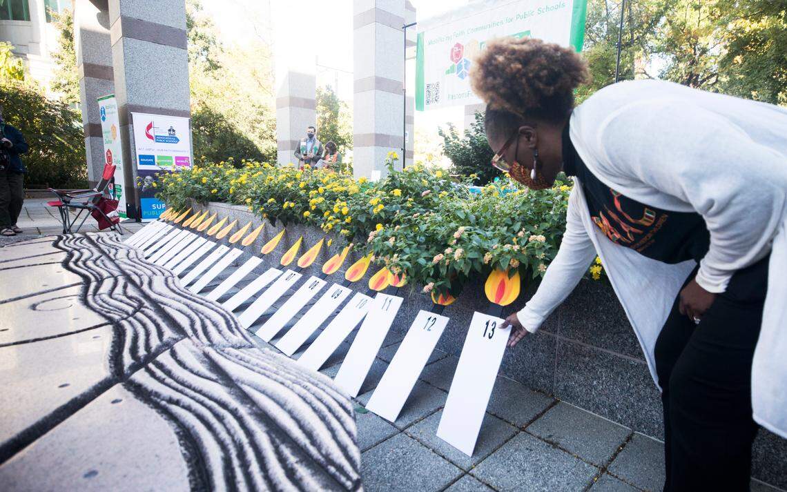During an Oct. 18, 2021 prayer vigil in Raleigh, Jovonia Lewis places a candle poster representing the year 2013 alongside others marking the decades-long Leandro court case on school funding. The case was initially filed in 1994 when school districts and families in five low-wealth counties sued the state to get more funding.