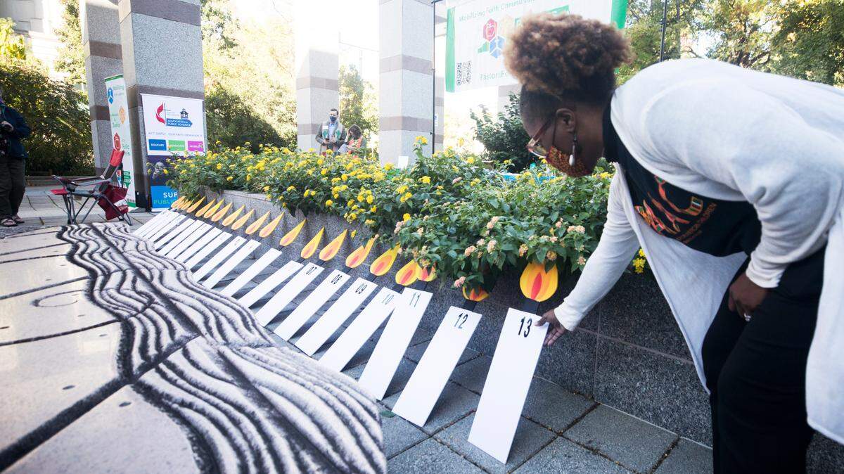 During an Oct. 18, 2021 prayer vigil in Raleigh, Jovonia Lewis places a candle poster representing the year 2013 alongside others marking the decades-long Leandro court case on school funding. The case was initially filed in 1994 when school districts and families in five low-wealth counties sued the state to get more funding.