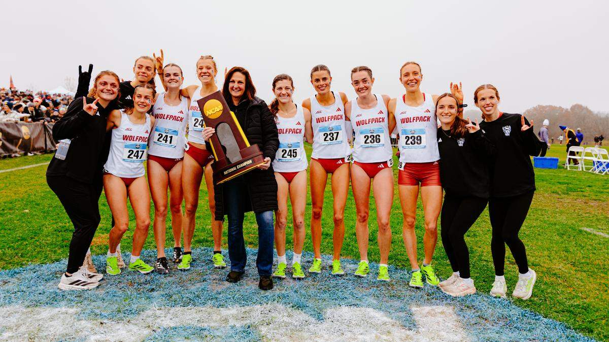 N.C. State women’s cross country coach Laurie Henes holds the national championship trophy as the Wolfpack celebrate after finishing first at the NCAA cross country championships at Columbia, Missouri, on Saturday, November 22, 2025.