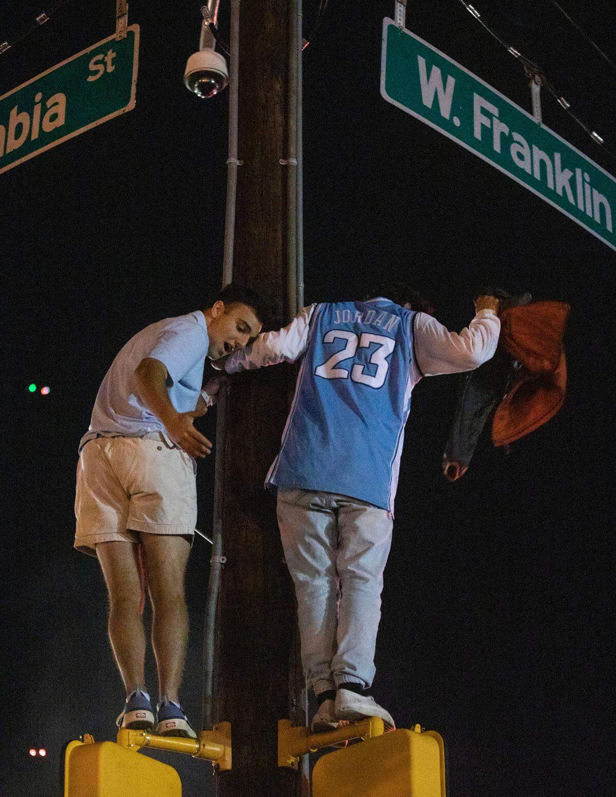 UNC Fans stand on crosswalk lights at the intersection of Franklin and Columbia Streets after a historic win against Duke in the Final Four on Saturday, April 2, 2022.